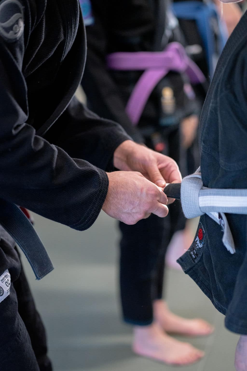 close up of The Jiu Jitsu Institute instructor tying new belt colors onto student
